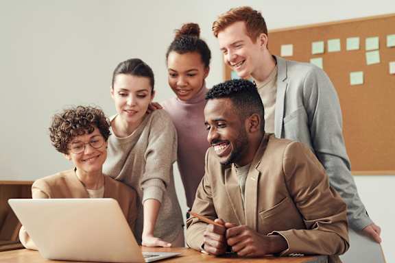 A group of five people are gathered around a laptop.