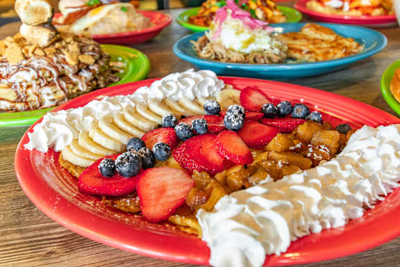 A red plate with whipped cream, strawberries, blueberries, and bananas.
