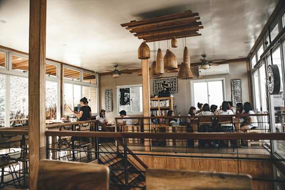 A group of people are sitting at tables in a restaurant with wooden chairs and tables.