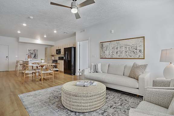 A living room with a white couch, a round ottoman, and a painting on the wall.