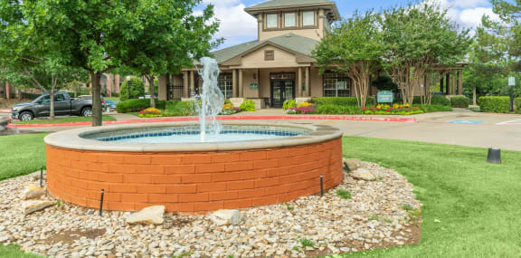 a fountain in the middle of a lawn in front of a house