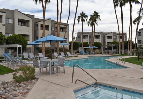 a swimming pool with chairs and umbrellas at an apartment complex