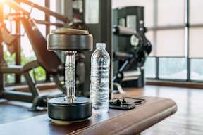 A bottle of water and a dumbbell on a bench in a gym.