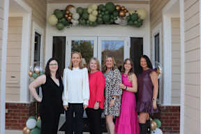 A group of women are standing in front of a house with balloons.