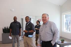 A man in a grey shirt is standing in a room with three other men.