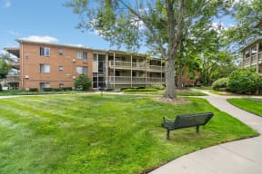 a park bench sits in the middle of a grassy area in front of an apartment building