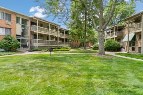 a grassy area with trees in front of an apartment building