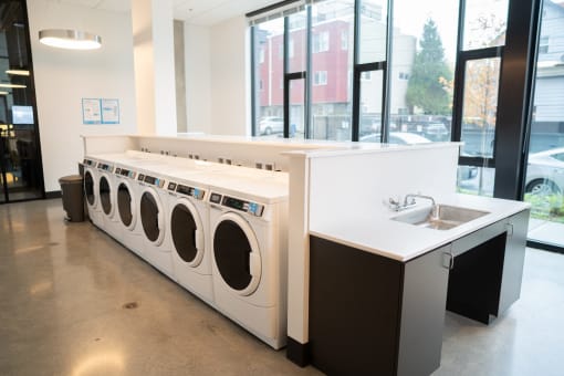 a row of washers and dryers in a laundromat with a sink
