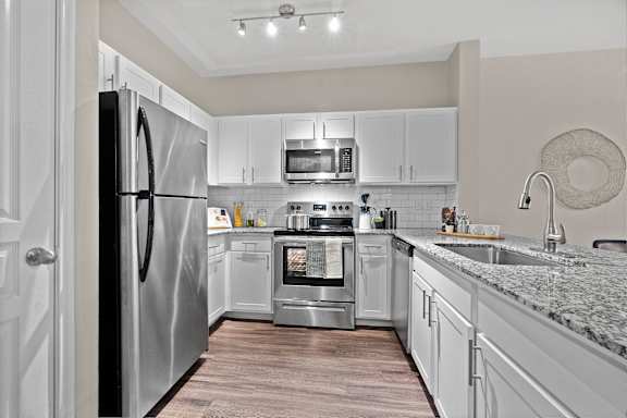 A kitchen with a refrigerator, oven, microwave, and sink.