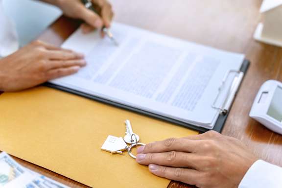 A person is signing a document with a set of keys on a clipboard.