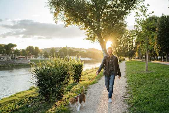 a man walking his dog down a path near a river