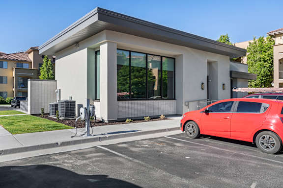 A red car is parked in front of a modern building with a charging station.