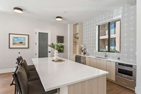 A modern kitchen with a white countertop and dark chairs.