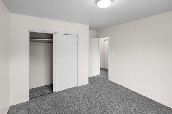A room with a grey carpet and white walls with a white door and a white cabinet.