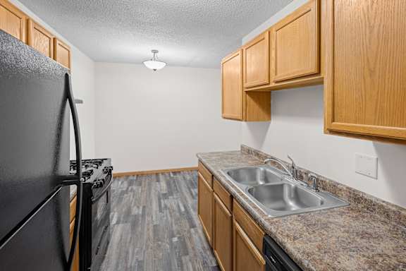 A kitchen with a black refrigerator and wooden cabinets.