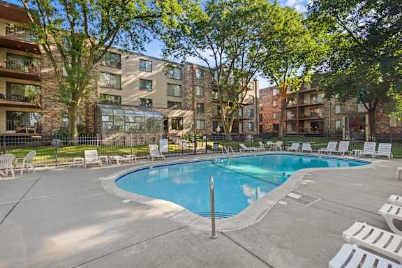 A swimming pool surrounded by lounge chairs and trees in front of apartment buildings.