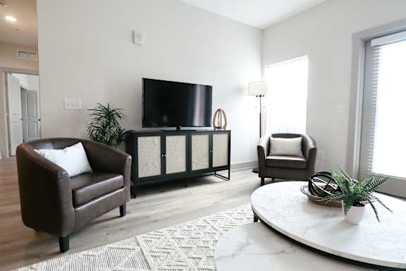 A living room with a brown leather chair, a flat screen TV, a round coffee table, and a cabinet with glass doors.