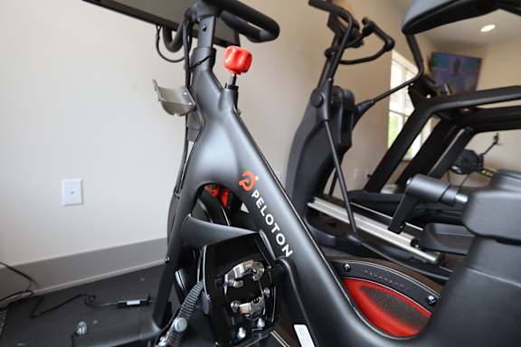 A Peloton bike is shown up close, with the brand name visible on the frame.