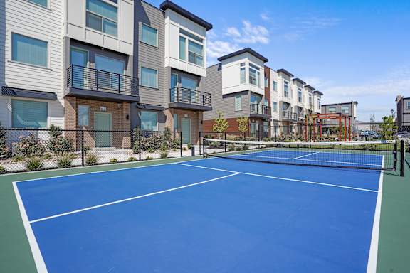 A tennis court is surrounded by apartment buildings.