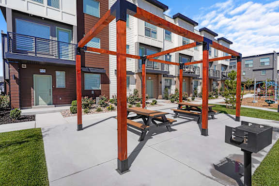 A wooden pergola with benches is in the foreground of a residential area.