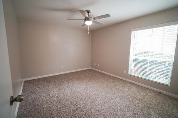 an empty bedroom with a ceiling fan and a window