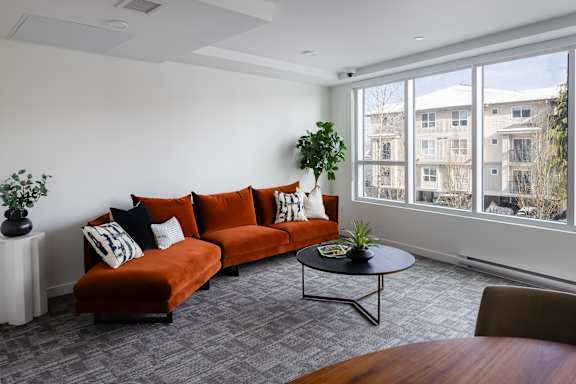 A living room with a red couch and a small table with a plant on it.
