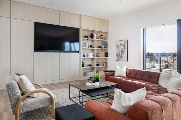 A modern living room with a grey sofa, a wooden chair, a black coffee table, and a flat-screen TV mounted on the wall.
