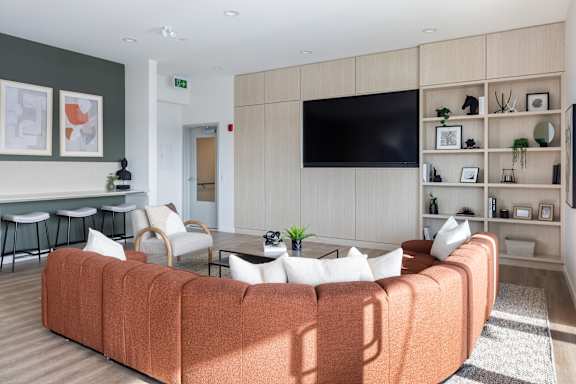 A living room with a large orange sofa and a flat screen TV mounted on the wall.