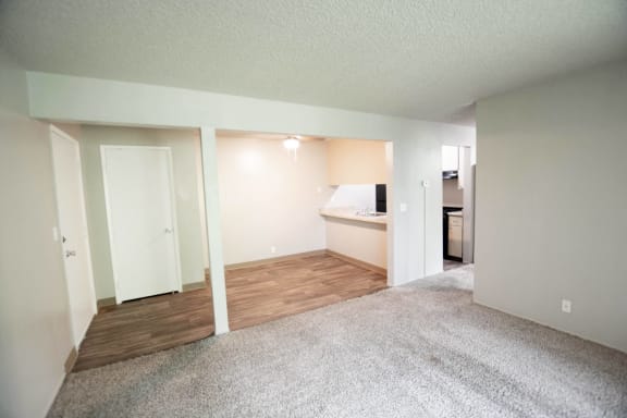 an empty living room with wood flooring and a kitchen