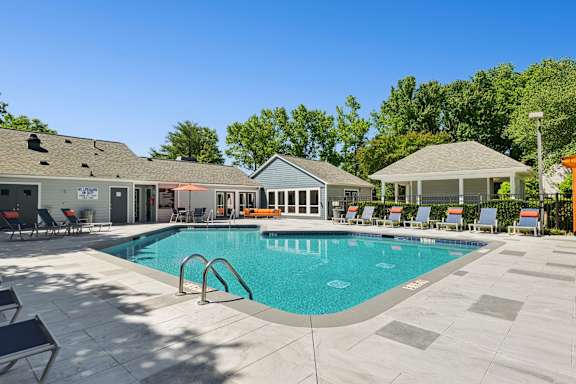 A swimming pool surrounded by a patio with chairs and a gazebo.