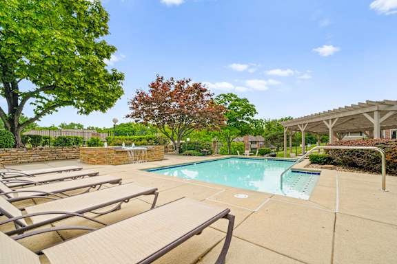 A pool surrounded by trees and chairs.