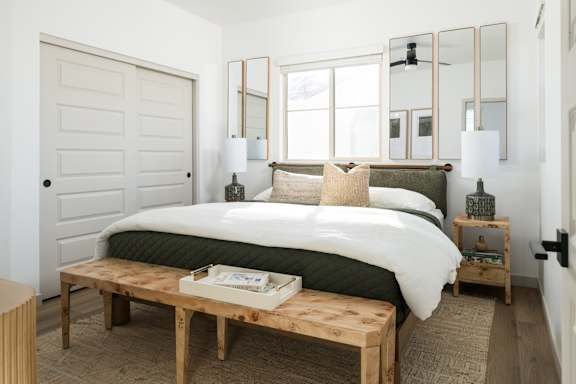 A bedroom with a bed, a bench, and a mirror on the wall.