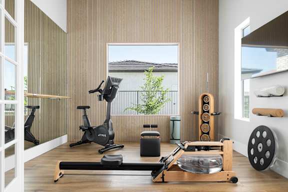 A home gym with a treadmill, rowing machine, and weights.
