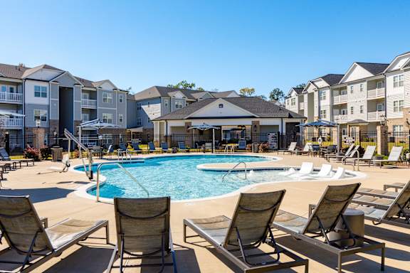 A pool surrounded by lounge chairs in front of apartment buildings.