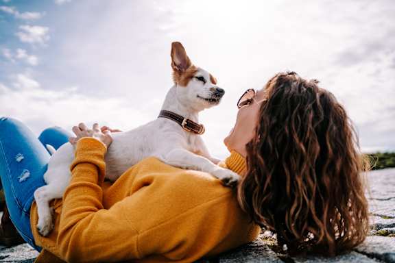 A woman in a yellow sweater is holding a small white dog with a brown collar.