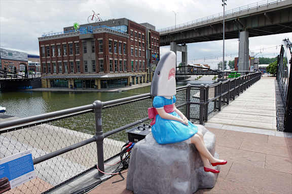 A girl in a blue dress is sitting on a rock by the water at The Lofts at Elk Terminal Apartments, Buffalo, NY 14204