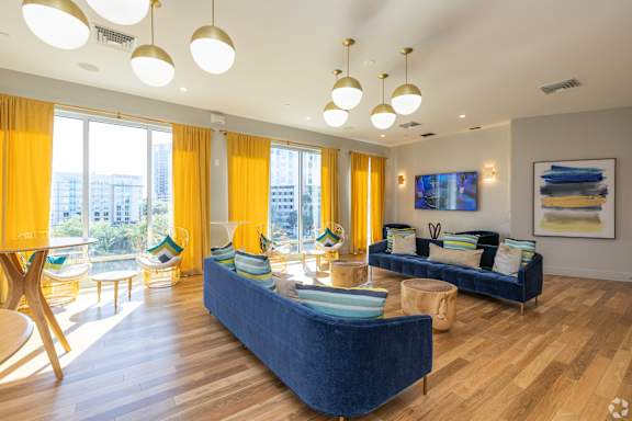 Resident lounge with two blue sofas, globe pendant lights, bistro tables and tall windows framed by yellow curtains.