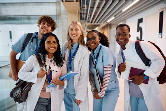 A group of five people in white lab coats stand together in a hallway.