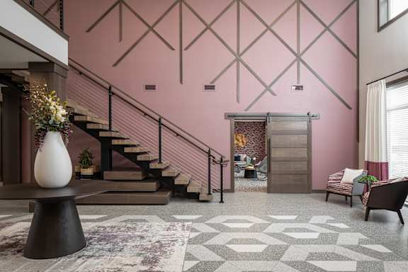 A living room with a staircase and a grey and white patterned rug.