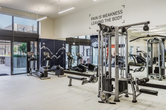 a gym with weights and cardio machines and a sign that reads pain is weakness leaving at SMB Hollywood Apartments, California