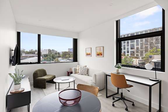 A living room with a white couch, a red table, and a large window.