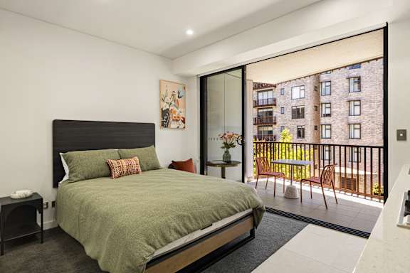 A bedroom with a large bed and a view of a building outside through a glass door.