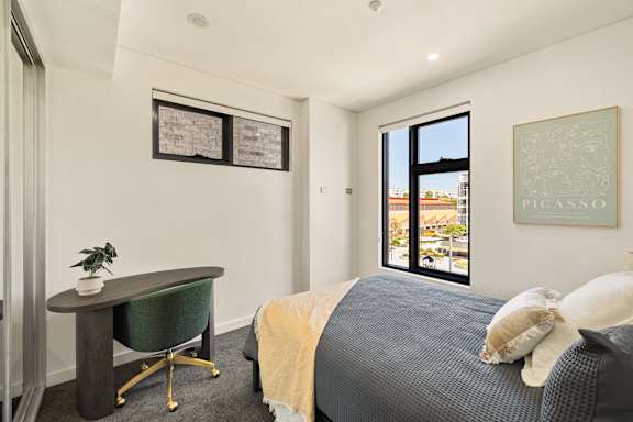 A bedroom with a bed, desk, and two framed pictures on the wall.