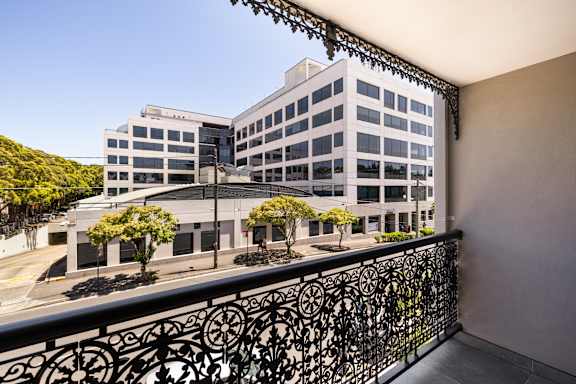 A balcony with a black railing overlooks a large white building with many windows.