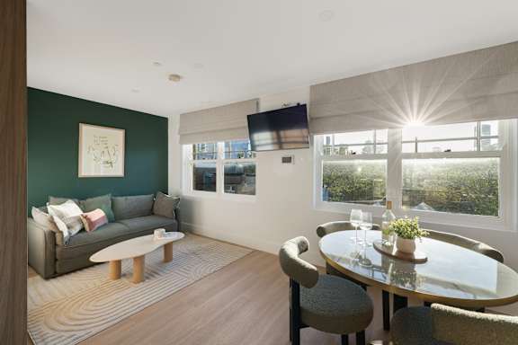 A modern living room with a grey couch, a glass table, and a television mounted on the wall.