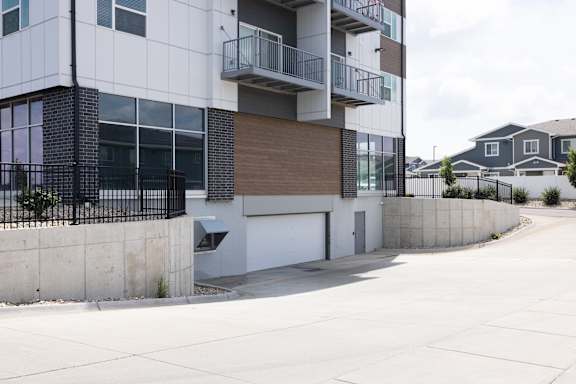 A modern apartment building with a white and brown facade and a black metal fence.