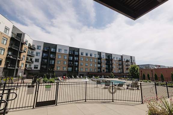 A black fence surrounds a pool area in front of a large apartment building.