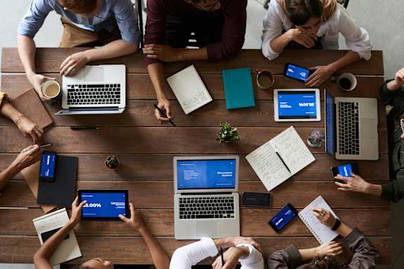 A group of people sitting around a table with laptops and tablets.