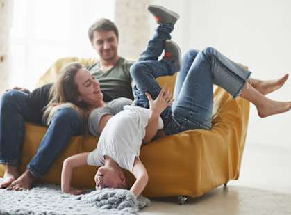 A family of three is having fun on a yellow couch.