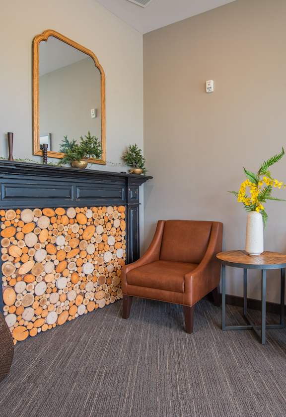 A room with a fireplace, two chairs, a table, and a vase of flowers.